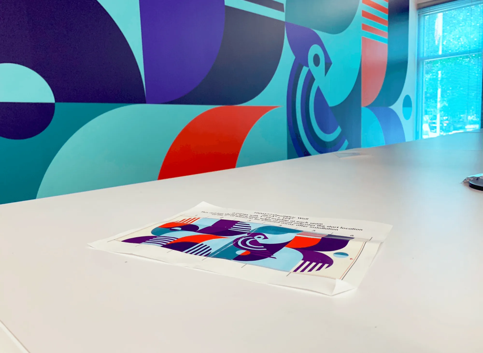 Close-up of the geometric mural on the office wall, with a printed proof of the design on a table
