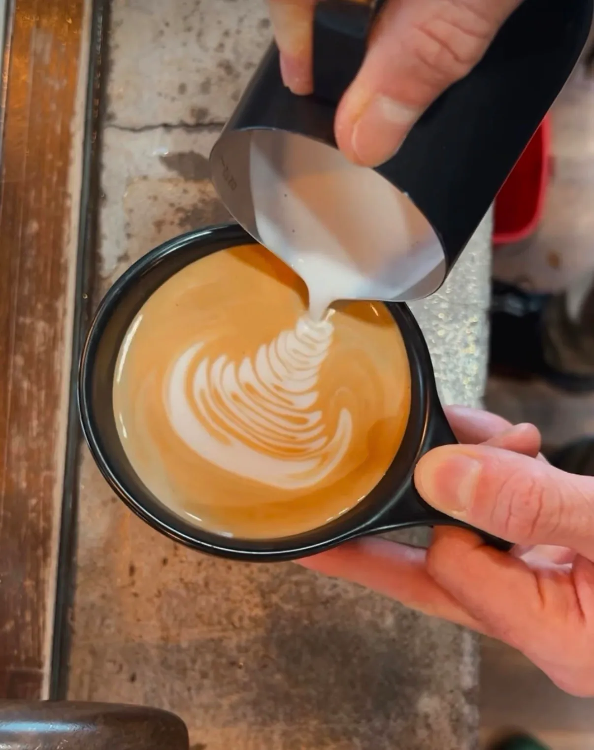 Barista pouring latte art into a black cup