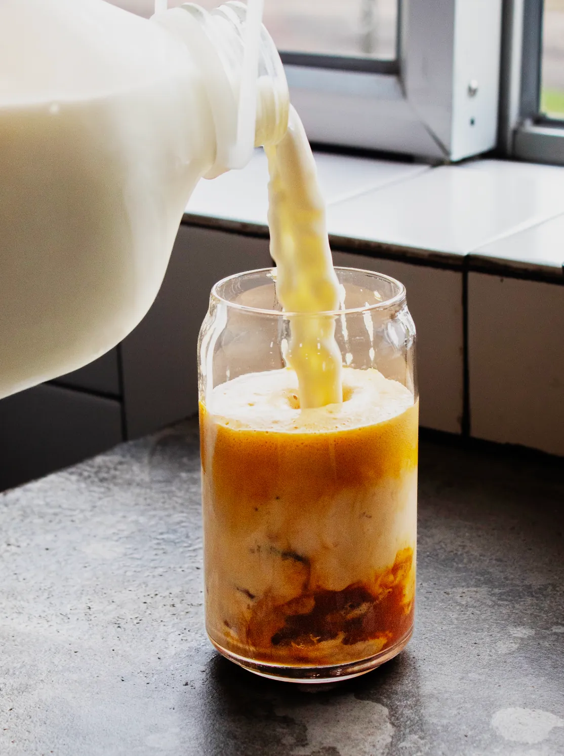 Milk being poured into an iced coffee in a glass can